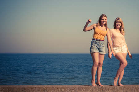 Two young women best friends blonde cheerful girls having fun outdoor by seaside. Summer happiness friendship concept.の写真素材