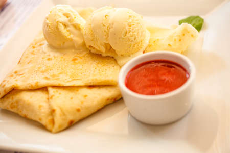 Pancake with ice cream and strawberry sauce on restaurant tableの写真素材