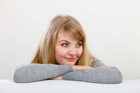 Dreaming and thinking concept. Lovely enjoyable smiling woman lying on back of sofa. Charming joyful attractive blonde girl portrait.の写真素材