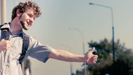 Young man hitchhiking on summer vacation. Happy guy tourist beside road with thumb up gesture having fun.の写真素材