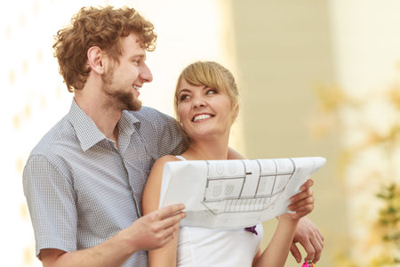 Real estate and family concept - young couple with blueprint project  building plans dreaming about...