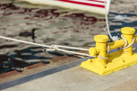 Yellow mooring bollard with blue rope in marina yachts in the background