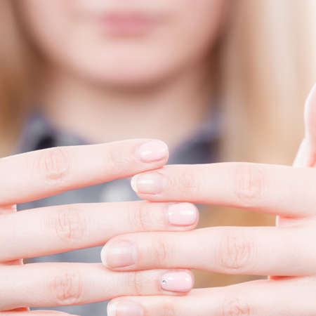 Manicure and hygiene concept. Blonde casual woman presents hands fingers. Girl with one hand coloured by hybrid nail polish and other without.の写真素材