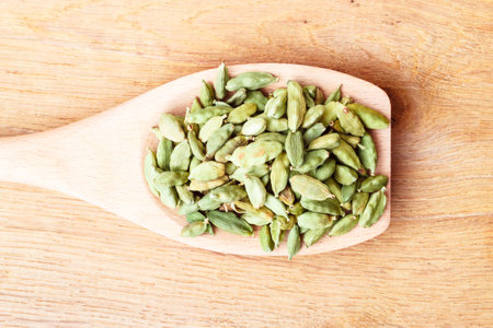 Green cardamom pods heap on wooden spoon rustic table backgroundの写真素材