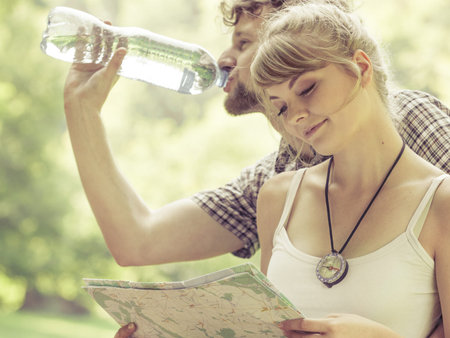 Adventure, tourism active lifestyle - young couple backpackers hikers resting in forest drinking...