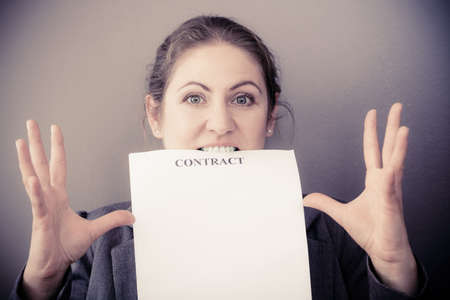 Stress at work. Contracts and agreements concept. Middle aged stressed angry upset business woman biting contract agreement. Face emotion expression. Human on deadline reaction.の写真素材