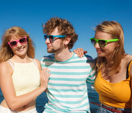 Friendship happiness summer holidays concept. Group of friends boy two girls in colorful sunglasses having fun outdoor against sky,  joy playful mood.の写真素材