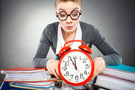 Corporate job workaholism time concept. Emotional secretary with clock. Nervous female office worker at desk with alarm ringer.の写真素材
