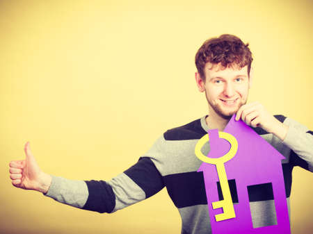 Good purchase concept. Male buyer with paper model of house and key. Smiling positive man buying his first real estate flat building.の写真素材