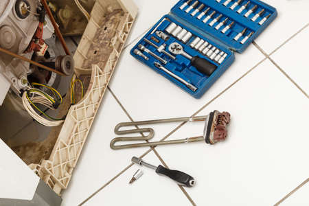 Mechanical industrial domestic electrical engineering concept. Washing machine during repair. Broken  with heater removed next to tool set.の写真素材