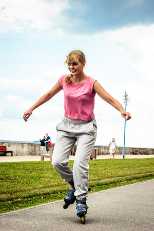 Active young woman in training suit rollerskating outdoor. Happy girl riding enjoying sport.