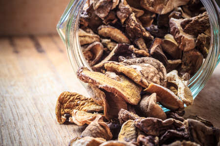 Food. Closeup dry mushrooms spilling out from storage jar on wooden surface table background.の写真素材