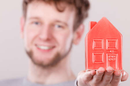 Symbolism housing safety family finances mortgage concept. Young man holding house on palm. Male presenting home model.の写真素材