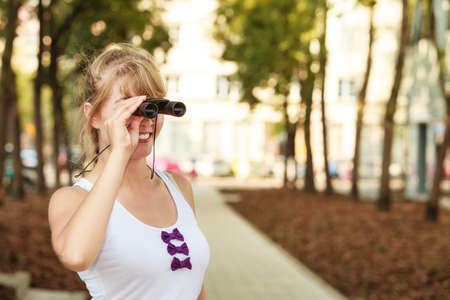 Summer holidays and tourism concept. Lovely tourist woman looking through binoculars n city, look forward with pleasure to travel.の写真素材