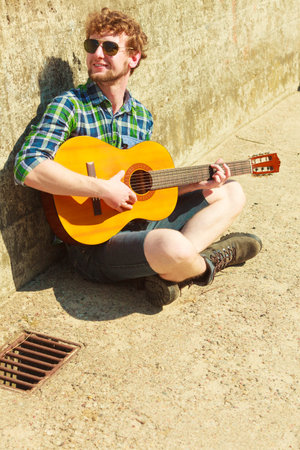 Music and people concept. Young bearded hipster man with guitar outdoor on street