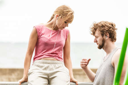 Woman and man with earphones listening to music outdoor. Young couple relaxing taking break from fitness exercise. Healthy lifestyle.の写真素材