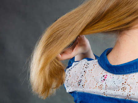 Everyday hygiene and care about good look. Back view of blonde casual girl combing her long straight hair. Woman using black comb hairbrush.の写真素材