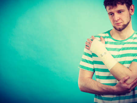 Pain and injury concept. Young man holds bandaged hand. Injured part of body. Medicine and healthcare.の写真素材