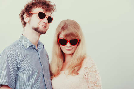 Happy young couple in heart shaped glasses. Smiling friends woman and man in studio.の写真素材