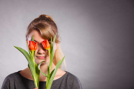 Beauty nature flora symbolism concept. Blonde girl blinded by flowers. Young female covering her eyes with tulips.の写真素材
