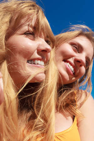 Two young women best friends blonde cheerful girls having fun outdoor against blue sky wind blowing in hair. Summer happiness friendship concept.の写真素材