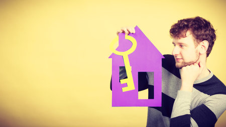 Dream about stabilization and family. Young man with paper house and big key. Dreaming boy full of plans ideas. New flat apartment.の写真素材