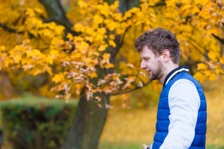 Season, happiness and people concept. Young bearded man walking relaxing in autumnal park on sunny day, yellow tree foliageの写真素材