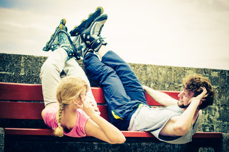 Young people friends in training suit with roller skates. Woman and man relaxing lying on bench...