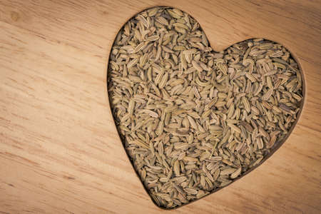 Dried fennel dill seeds heart shaped on wooden surfaceの写真素材