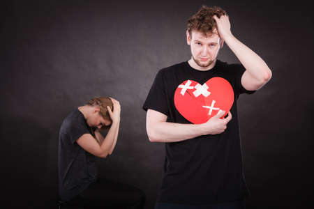 Broken heart difficult love concept. Sad unhappy couple woman and man holding paper red heart fixed with plaster bandage. Rift in relations.の写真素材