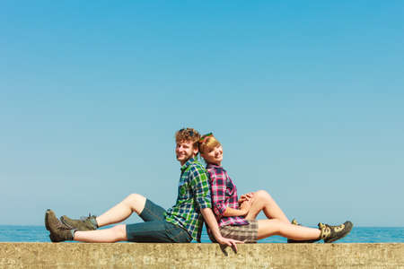 Summer vacation and traveling concept. Young hiking couple woman man relaxing after hike on sea shore enjoying sunlightの写真素材