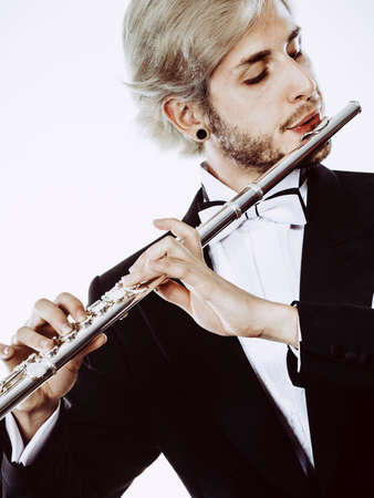 Classical music study concept. Male flutist musician performer playing flute. Young elegant man wearing tailcoat holds instrumentの写真素材