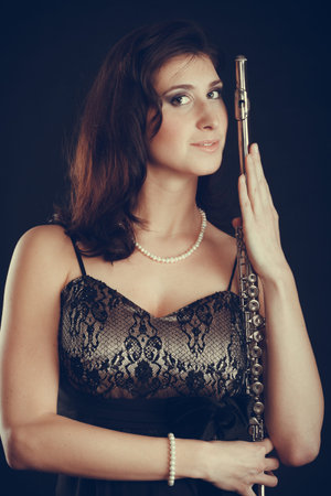 Music performance. Stunning elegant young lady with transverse flute instrument on black. Woman preparing to her solo show in theater opera.の写真素材