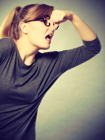 Filth hygiene dirt trash garbage concept. Nerdy girl holding nose. Young blonde in glasses pinching to stop odor. Bad disgusting smell.の写真素材