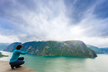 Tourism and travel. Woman tourist taking photo with camera, enjoying mountains fjords view in Sogn og Fjordane county. Norway Scandinavia.の写真素材