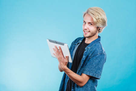 Education social media. Modern technology internet concept. Stylish handsome young guy using tablet computer, on blue colorの写真素材