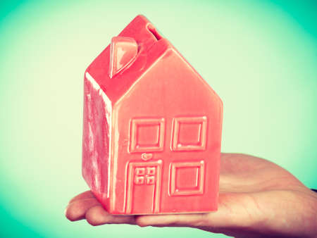First flat apartment. Step forward concept. Male hand holding little small red house home. Part body man with idea of growing up.の写真素材