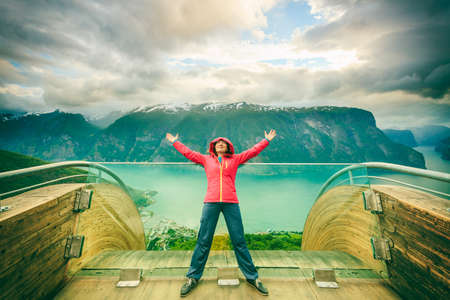 Tourist woman on Stegastein viewpoint enjoying Aurland fjord view with arms raised outstretched up, Sogn Og Fjordane, Norwayの写真素材