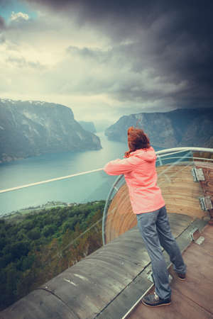 Tourist woman on Stegastein viewpoint enjoying Aurland fjord view in evening time, Sogn Og Fjordane, Norwayの写真素材