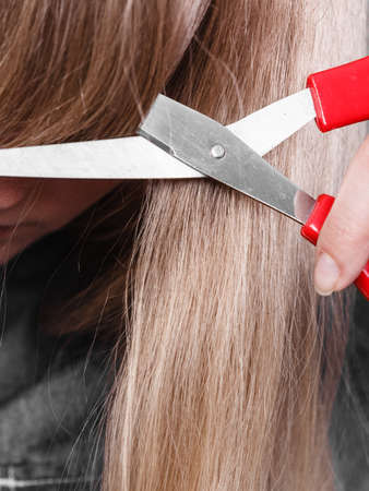 Little look change concept. Young blonde woman cutting down shearing her fringe short front hair. Girl using big scissors.の写真素材