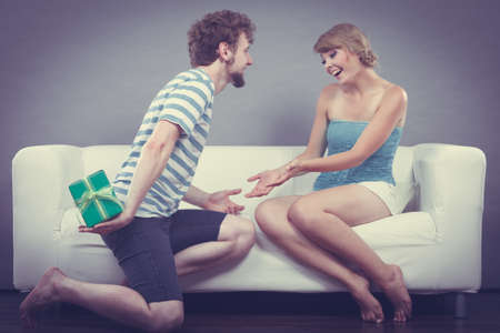 Couple sitting on couch at home. Young man giving woman gift box filtered photoの写真素材