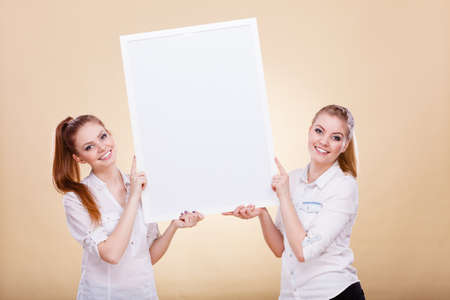 Advertisement concept. Teenage smiling girls holding blank presentation board. Young women showing banner sign billboard copy space for textの写真素材
