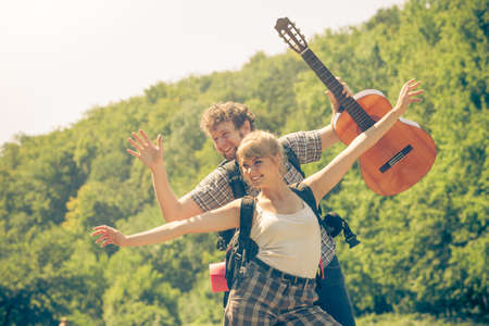 Adventure, tourism, enjoying summer time together - young couple tourists hikers with guitar having fun open arms outdoorの写真素材
