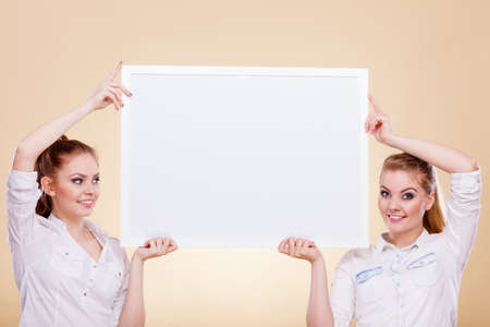 Advertisement concept. Teenage smiling girls holding blank presentation board. Young women showing banner sign billboard copy space for textの写真素材