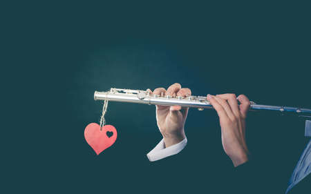 Valentines day love melody concept. Flute music playing man flutist musician performer. Male hands with instrument and red heart, close upの写真素材