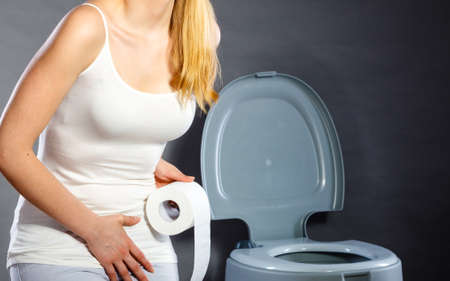 Sick woman with hands pressing her crotch lower abdomen, holding paper roll in front of toilet bowl. Medical problems, incontinence, health care conceptの写真素材