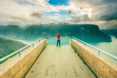 Tourism and travel. Woman tourist nature photographer taking photo with camera, enjoying Aurland fjord landscape from Stegastein lookout, Norway Scandinavia.の写真素材
