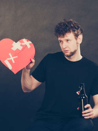 Addiction and trouble of drinking. Young man with bottle of alcohol on dark background. Broken heart and sadness concept.の写真素材