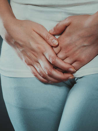 Closeup young sick woman with hands holding pressing her crotch lower abdomen. Medical or gynecological problems, healthcare conceptの写真素材