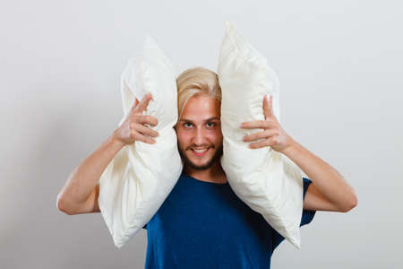 Sleeping well concept. Happy young man rested after good night sleep playing with pillows, smiling having funの写真素材
